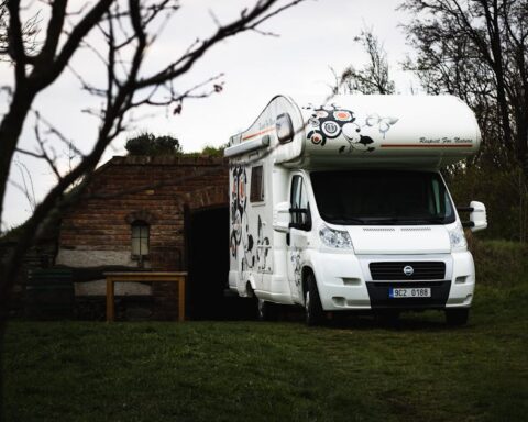 carado - A white Fiat camper parked near a rustic brick shed in a rural landscape.